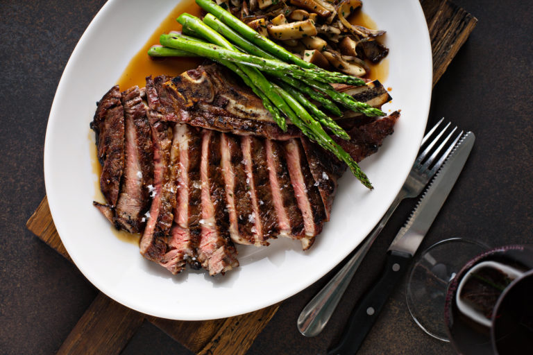 Cast-iron ribeye steak with asparagus, sliced mushrooms and pan juices on a white plate