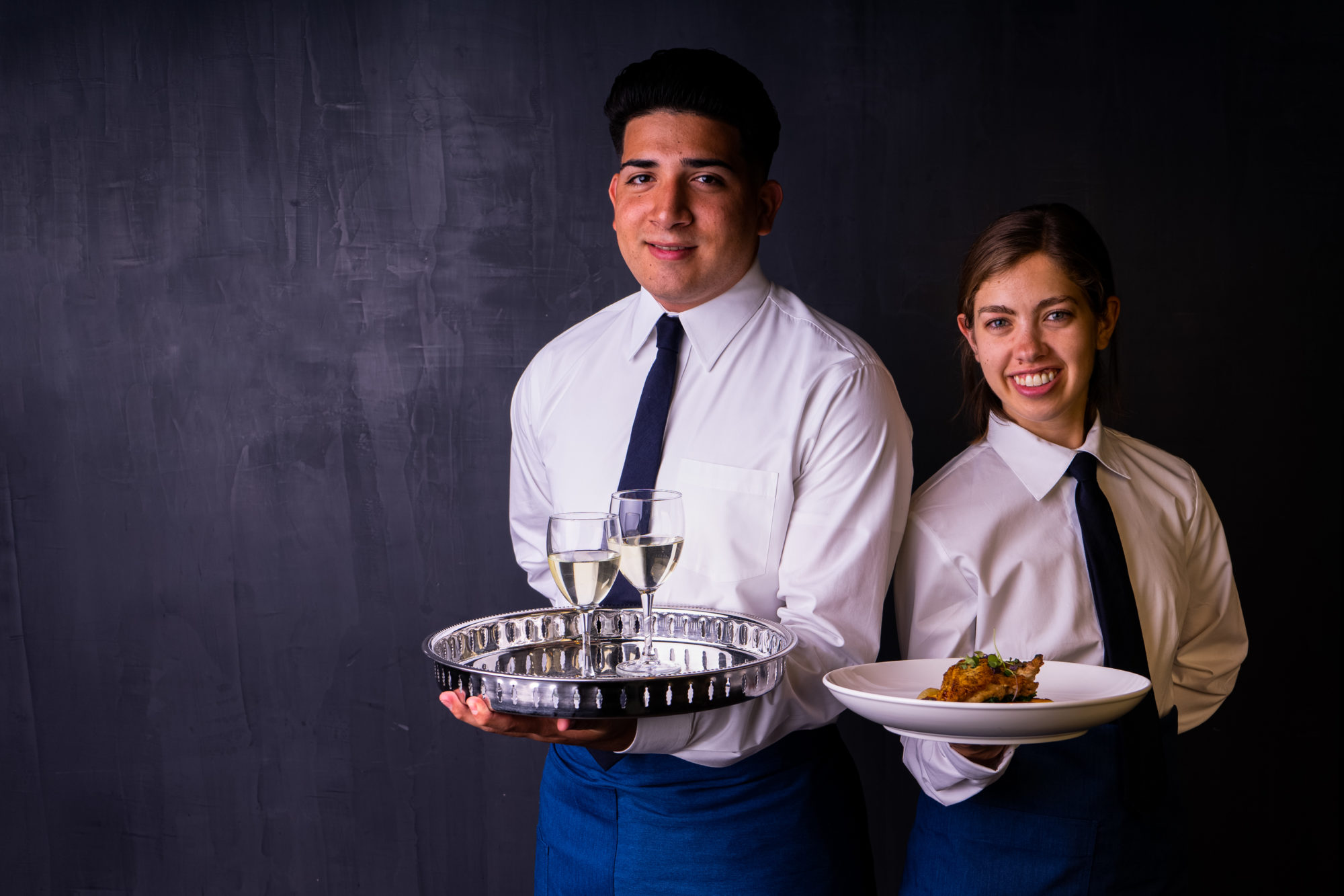 Two smiling servers offering beverages and food.