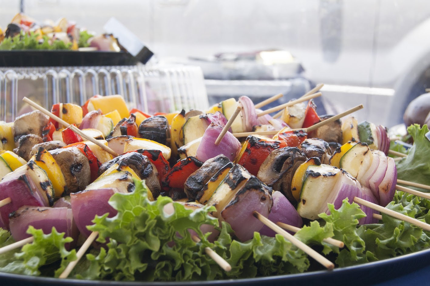 Multiple meat and vegetables Kabobs on a lettuce leaf on a tray.