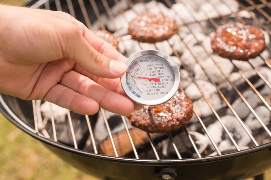 Someone taking the temperature of a burger patty on a grill.