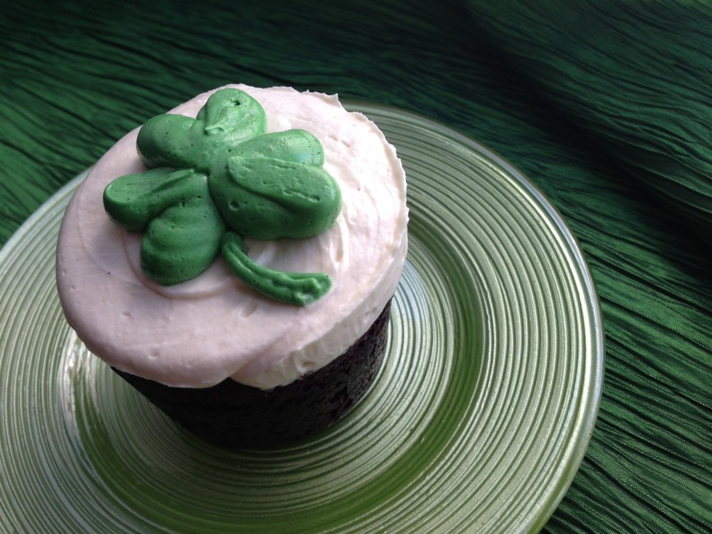 A chocolate cupcake with pink frosting and a green clover on top, placed on a green plate.