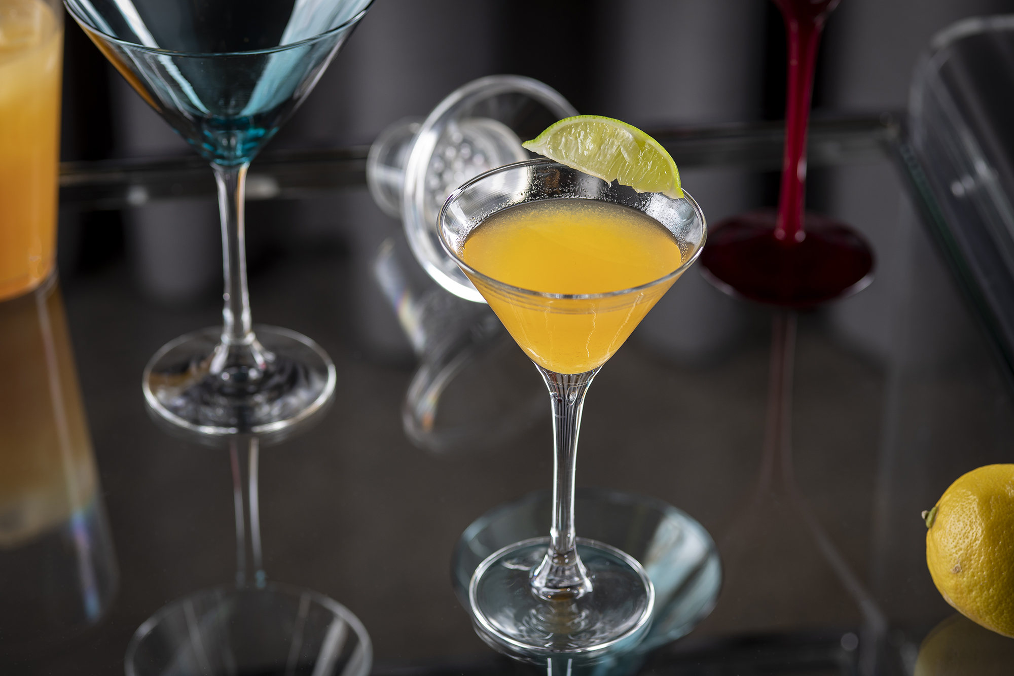 Bright yellow cocktail in a martini glass with a lime wedge garnish