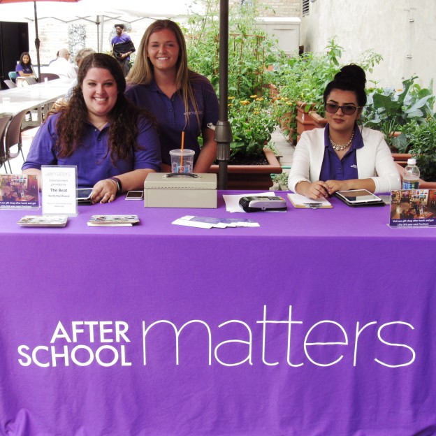 Three smiling women at a registration table that reads, "After School Matters"