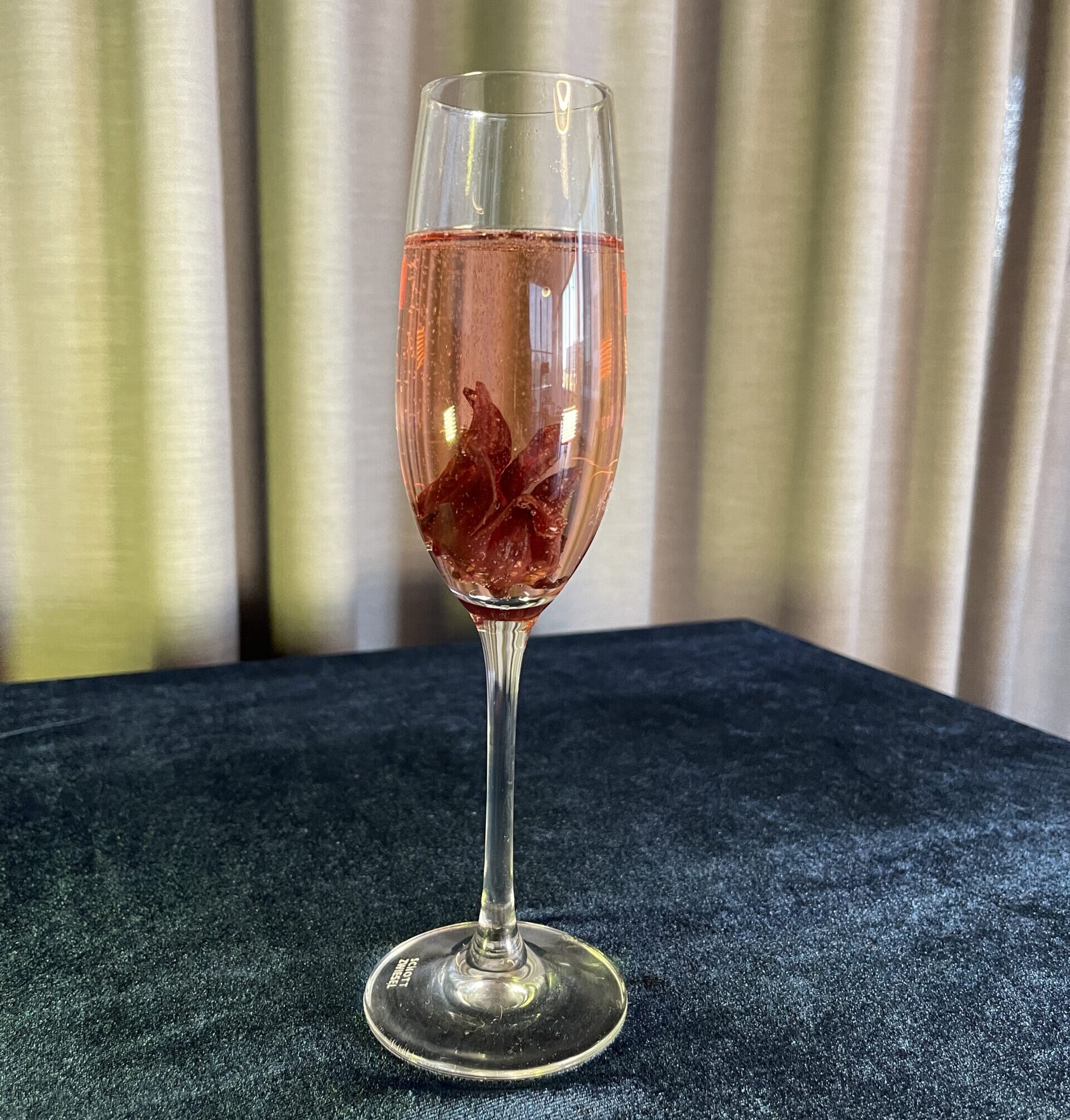 A cocktail in a champagne flute, garnished with an edible hibiscus flower.