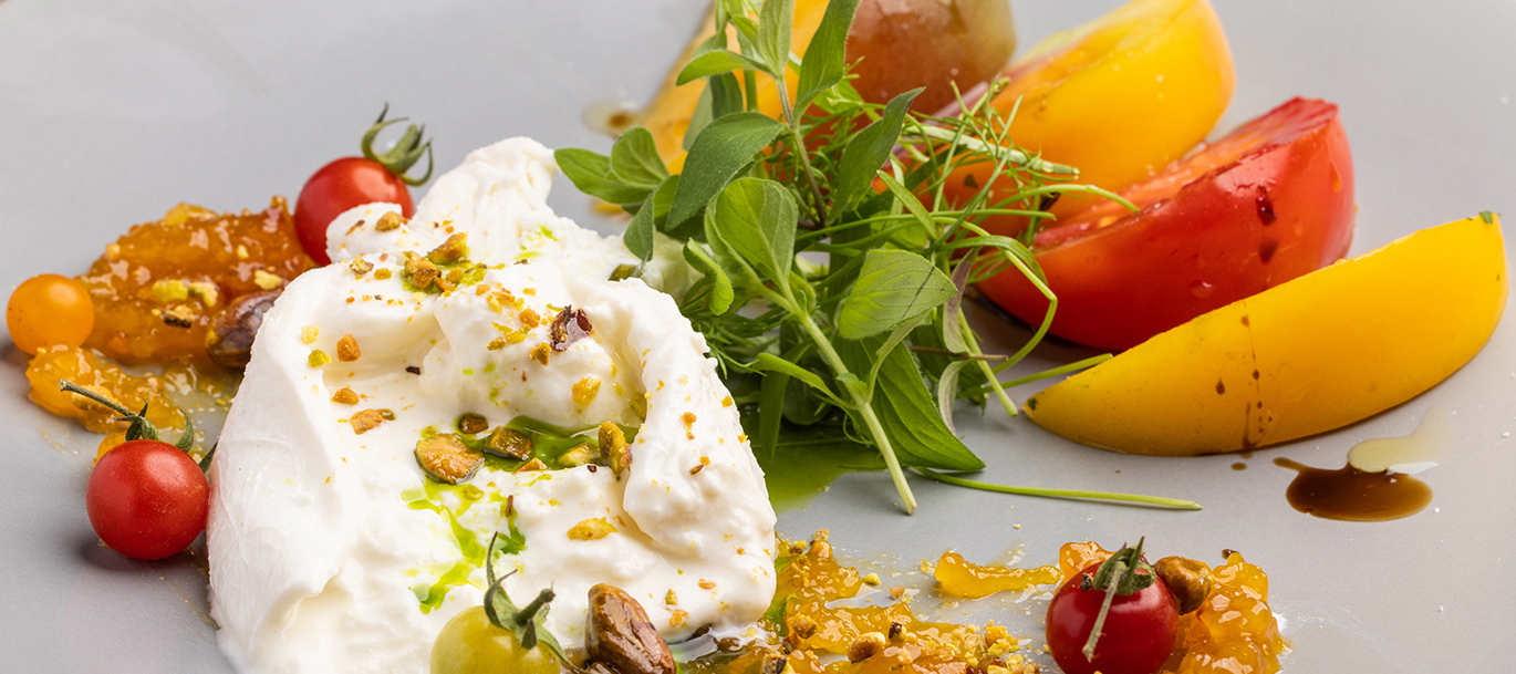 Image of an heirloom tomato salad with a generous serving of creamy burrata, and sprinkled with seasoning.